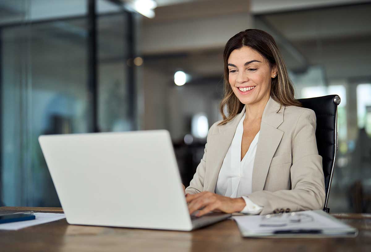 Happy mature business woman entrepreneur in office using laptop at work, smiling professional middle aged 40 years old female company executive wearing suit working on computer at workplace.